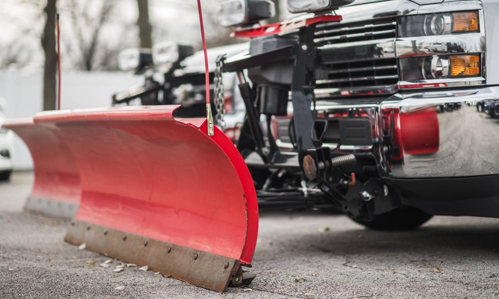 Two clean red snow plows are parked in an area where the snow has been cleared out and the drivers are not present.