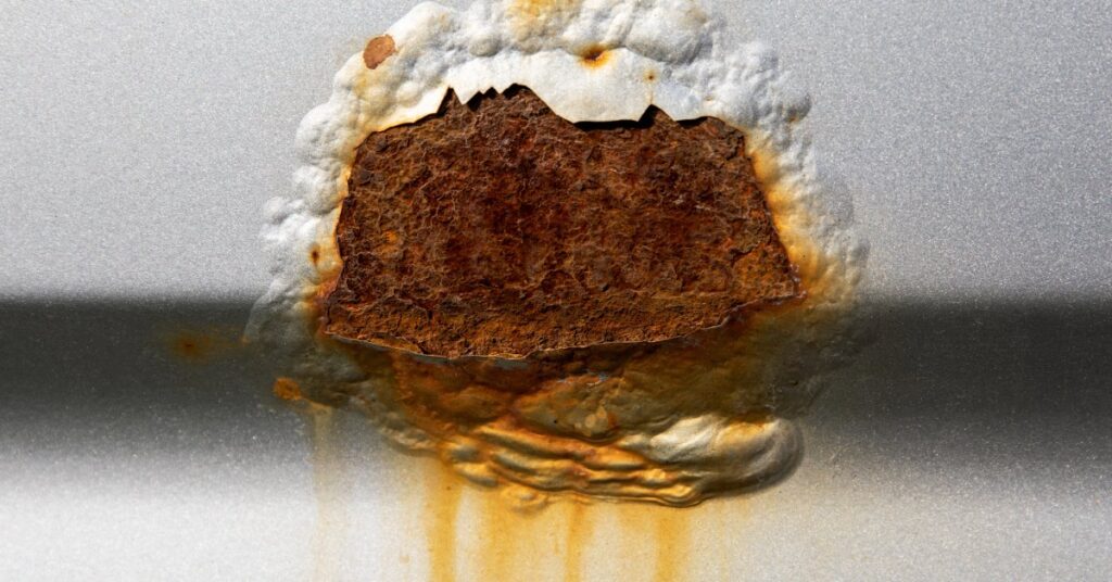 A massive cut on the side of a white vehicle that is covered in rust and surrounded by bubbling paint.