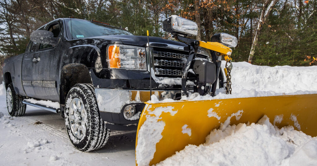 There is a pickup truck parked on a snowy road with a pile of snow sitting in front of its snow plow attachment.