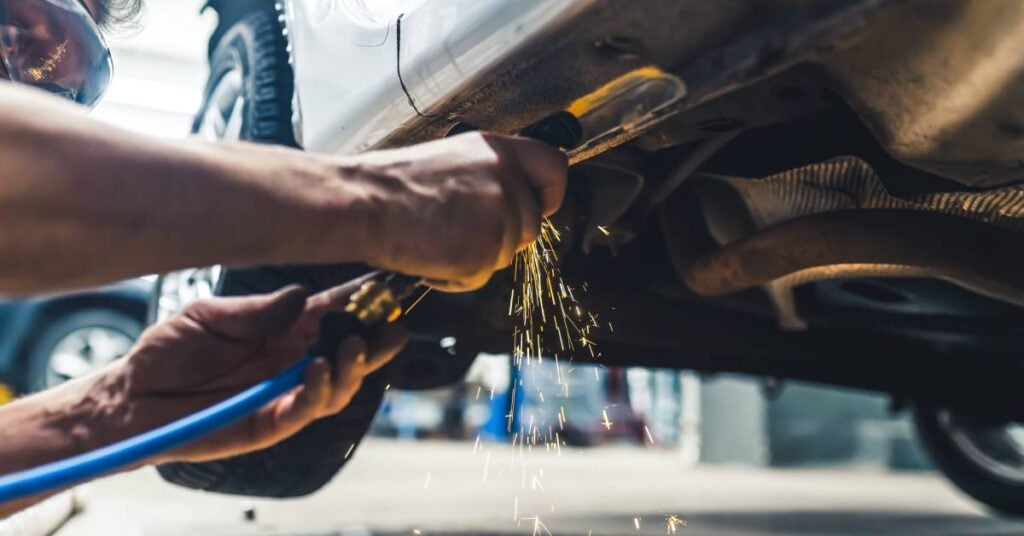 Sparks are coming out of an angle grinder a worker is using on a car. The worker uses two hands to control the grinder.