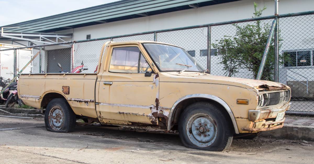 A yellow truck rests within a fenced lot. It has rust on the lower front of its passenger door and along the vehicle's trim.
