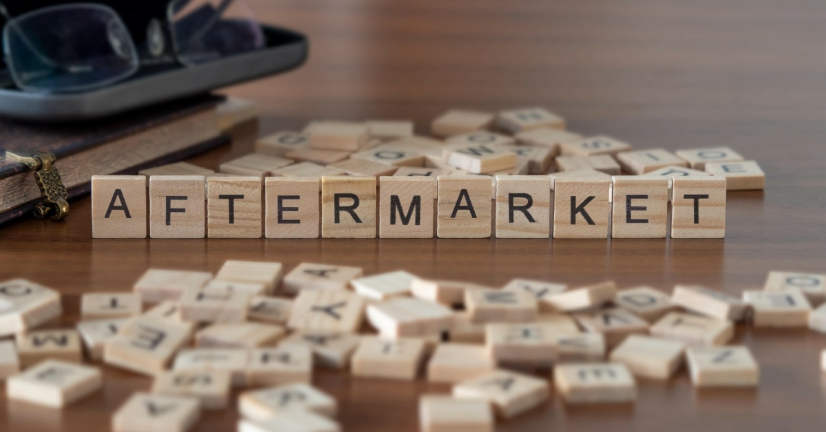 Alt Text: Two piles of letter tiles spread out on a wooden table. The letters that are standing up spell "aftermarket."