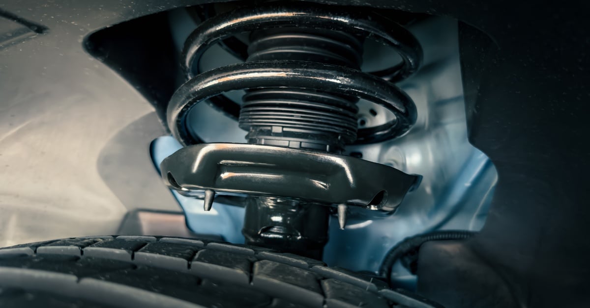 A car's suspension system contains a shock absorber strut with a coil spring. The car's black wheels are also visible.