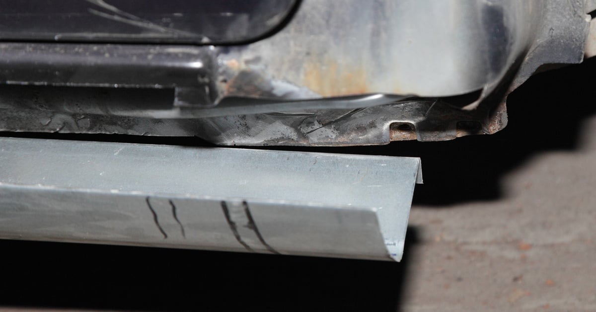 A grey rocker panel sits below a vehicle's body, waiting to be attached. The rocker panel's color matches the vehicle's body.