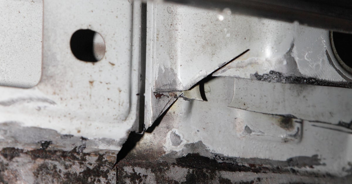 A close-up of a vehicle’s rusted rocker panel where corrosive metal destruction is widespread at the bottom of the rocker panel.