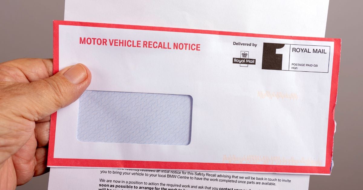 A hand holds a close-up of an envelope with "Motor Vehicle Recall Notice" written in red capital letters along with the document.