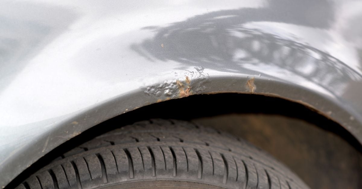 A close-up of small rust spots and bubbling paint on a silver vehicle above the wheel well and tire.