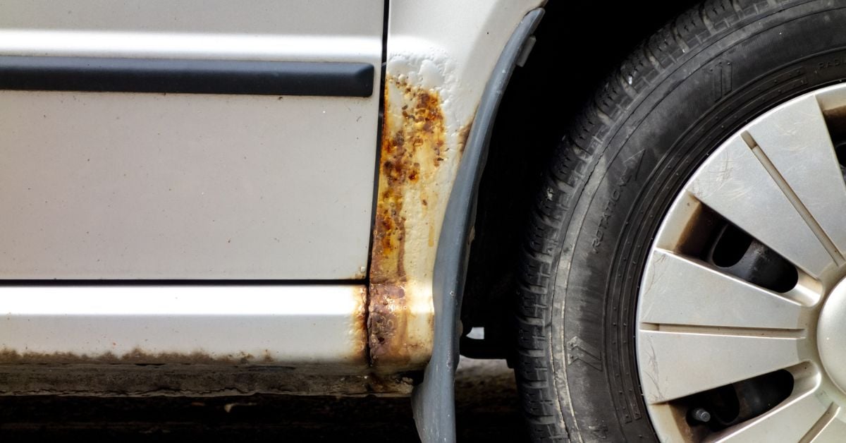 A close-up of the silver vehicle with significant rust and corrosion near the wheel mudguard and on the rocker panel.