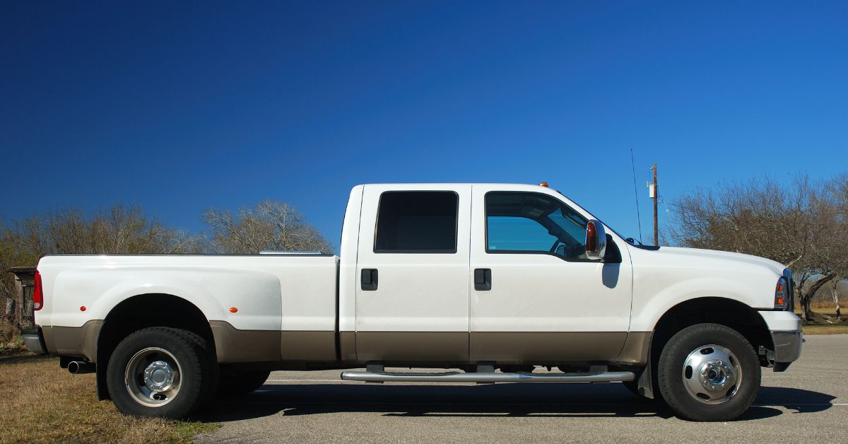 A horizontal view of a parked four-door white pickup truck with tinted back windows with a clear blue sky behind.