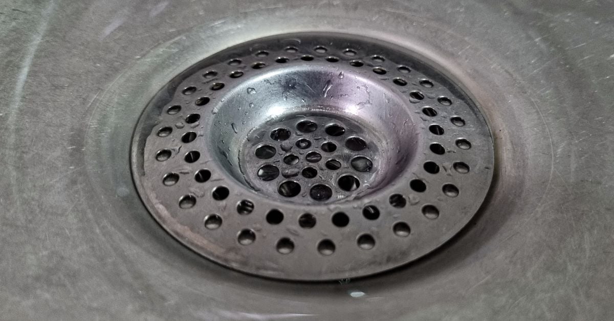 A close-up of a drain screen with many small holes in a stainless steel sink covered with water droplets.