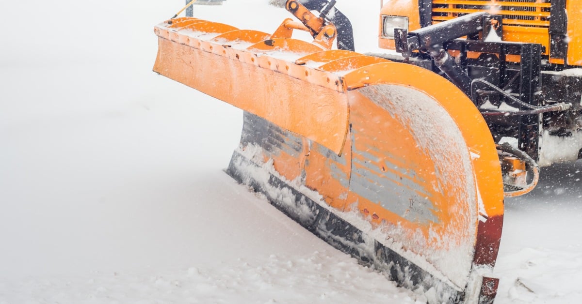 A closeup of the moldboard of a snow plow truck sitting on top of snow, with the orange paint chipping away.