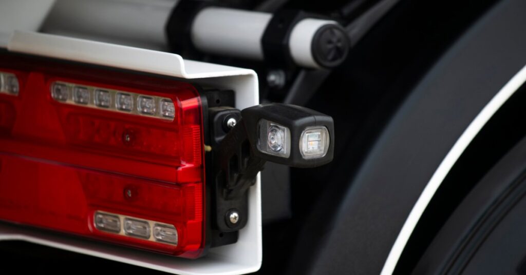 A close-up of a red vehicle tail light and rear body panel with smooth reflections and black-and-white trim.