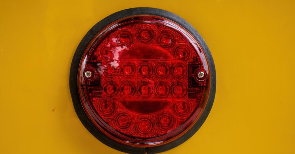 A red LED taillight mounted on a yellow vehicle body, shown close-up with a black rim and textured lens.