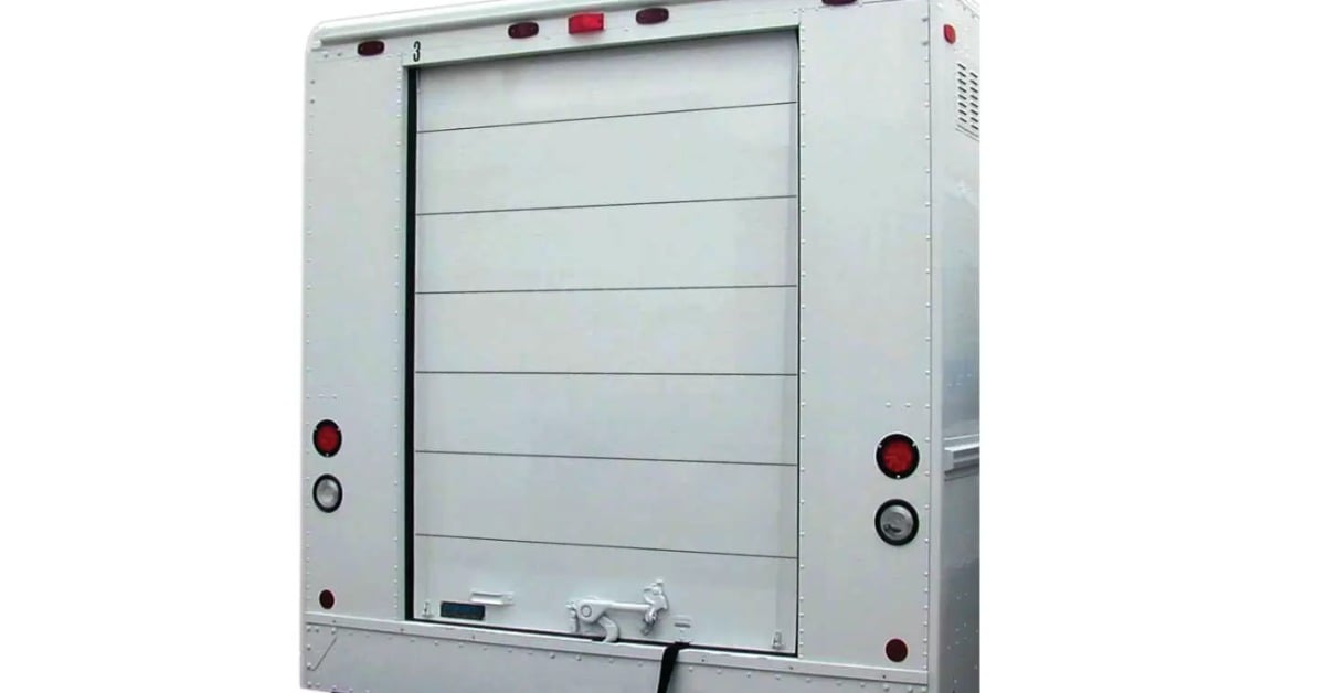 The rear view of a white step van, showing whiting style roll-up doors with a lock at the bottom area.